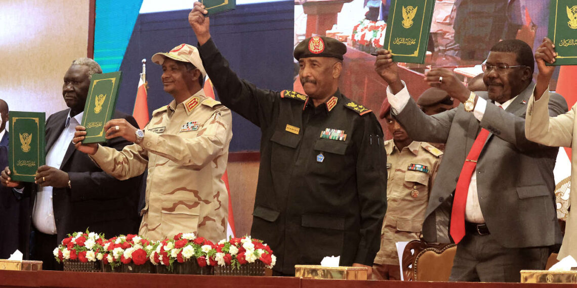 Sudan's Army chief Abdel Fattah al-Burhan (C R) and paramilitary commander Mohamed Hamdan Dagalo (C L) lift documents alongside civilian leaders following the signing of an initial deal aimed at ending a deep crisis caused by last year's military coup, in the capital Khartoum on December 5, 2022. - The past year has seen near-weekly protests and a crackdown that pro-democracy medics say has killed at least 121, a spiralling economic crisis exacerbated by donors slashing funding, and a resurgence of ethnic violence in several remote regions. Divisions among civilian groups have deepened since the coup, with some urging a deal with the military while others insist on "no partnership, no negotiation". (Photo by ASHRAF SHAZLY / AFP)