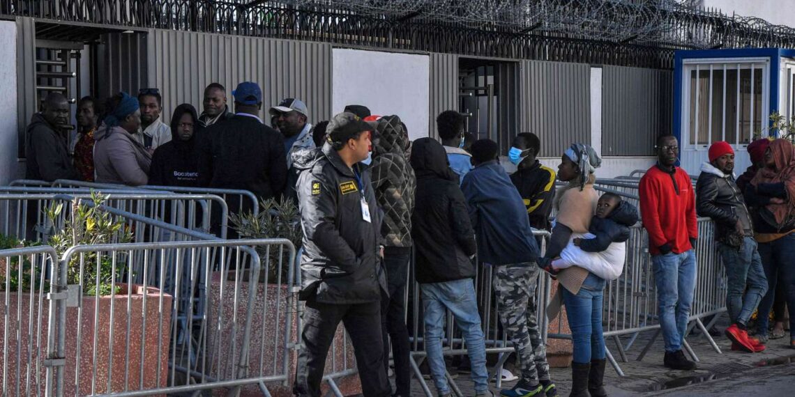 A security guard looks on as sub-Saharan African migrants gather outside the officers of the United Nations High Commissioner for Refugees (UNHCR) in Tunis on February 27, 2023, demanding a resolution of their situation. Tunisia's president was accused on February 22 of racism and hate speech after he said "hordes" of sub-Saharan African migrants were causing crime and posed a demographic threat. Saied, who has seized almost total power since a dramatic July 2021 move against parliament, had urged his national security council to take "urgent measures" to tackle irregular migration. (Photo by FETHI BELAID / AFP)