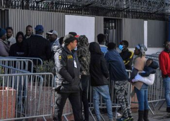 A security guard looks on as sub-Saharan African migrants gather outside the officers of the United Nations High Commissioner for Refugees (UNHCR) in Tunis on February 27, 2023, demanding a resolution of their situation. Tunisia's president was accused on February 22 of racism and hate speech after he said "hordes" of sub-Saharan African migrants were causing crime and posed a demographic threat. Saied, who has seized almost total power since a dramatic July 2021 move against parliament, had urged his national security council to take "urgent measures" to tackle irregular migration. (Photo by FETHI BELAID / AFP)