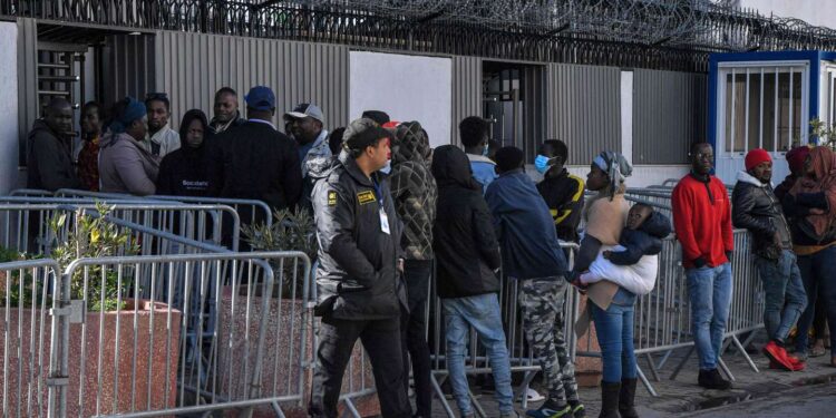 A security guard looks on as sub-Saharan African migrants gather outside the officers of the United Nations High Commissioner for Refugees (UNHCR) in Tunis on February 27, 2023, demanding a resolution of their situation. Tunisia's president was accused on February 22 of racism and hate speech after he said "hordes" of sub-Saharan African migrants were causing crime and posed a demographic threat. Saied, who has seized almost total power since a dramatic July 2021 move against parliament, had urged his national security council to take "urgent measures" to tackle irregular migration. (Photo by FETHI BELAID / AFP)