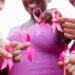 Cropped view of a multi-ethnic group of women of mixed ages standing together outdoors, wearing pink, at a breast cancer awareness rally, raising money to find a cure. They are each holding a breast cancer awareness ribbon. The focus is on their hands.